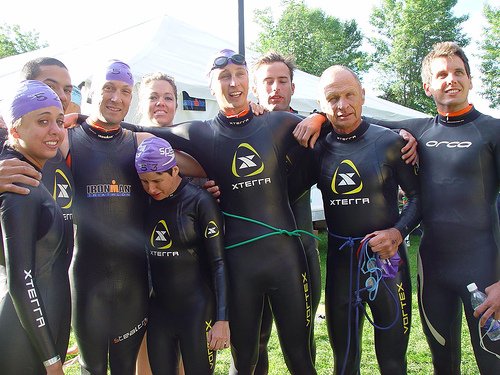 A race team gathered in wetsuits before a triathlon swim.